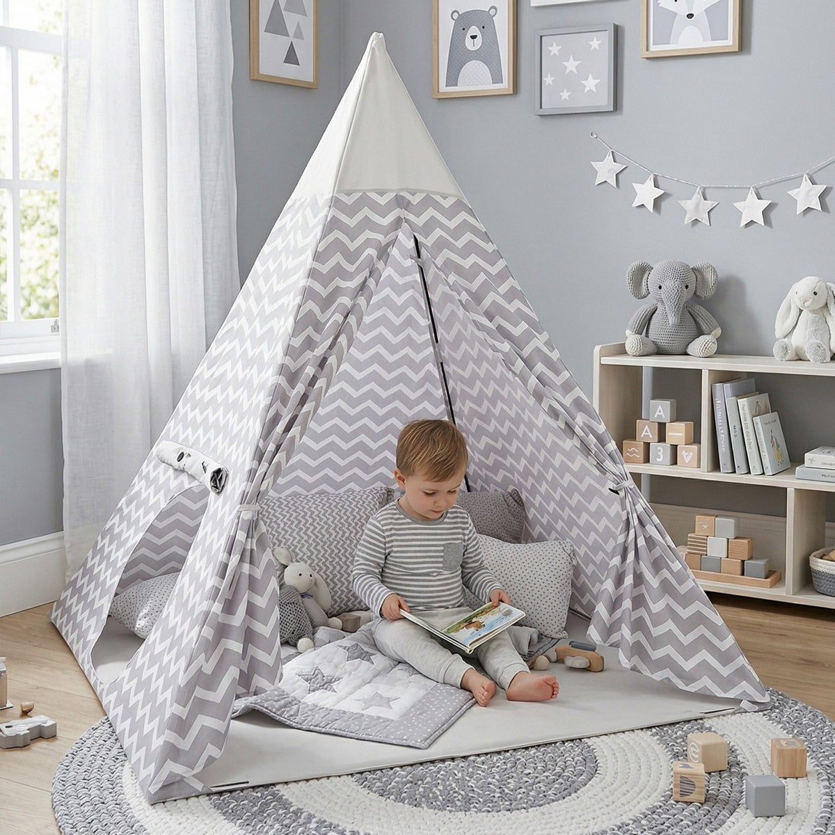 Niño sentado leyendo un libro dentro de una tipi gris y blanca decorada con cojines, en una habitación infantil de tonos neutros - Tufan