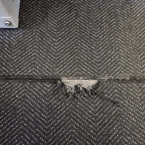 torn or worn black carpet or rug in floor of airplane