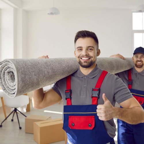 Portrait of smiling male movers carry carpet recommend good quality delivery or transportation service. Happy deliverymen or carriers help customer with moving or relocation. Shipping.